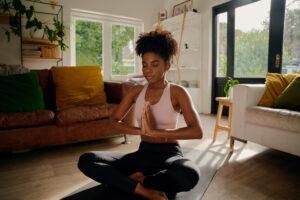 Junge Frau sitzt in Lotusposition mit verbundenen Händen auf Yogamatte und praktiziert Atemübungen.