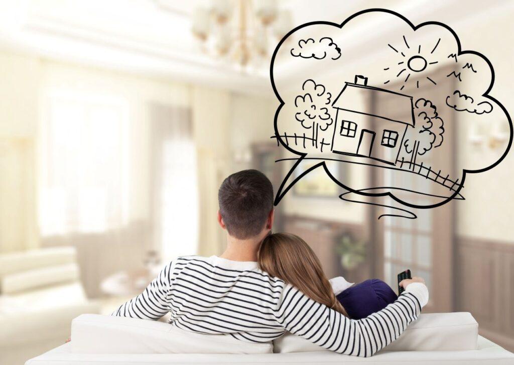 Ein junges Paar sitzt auf dem Sofa und träumt von einem Eigenheim – jetzt mit Immobilienmakler Neustadt in Holstein das perfekte Haus finden.