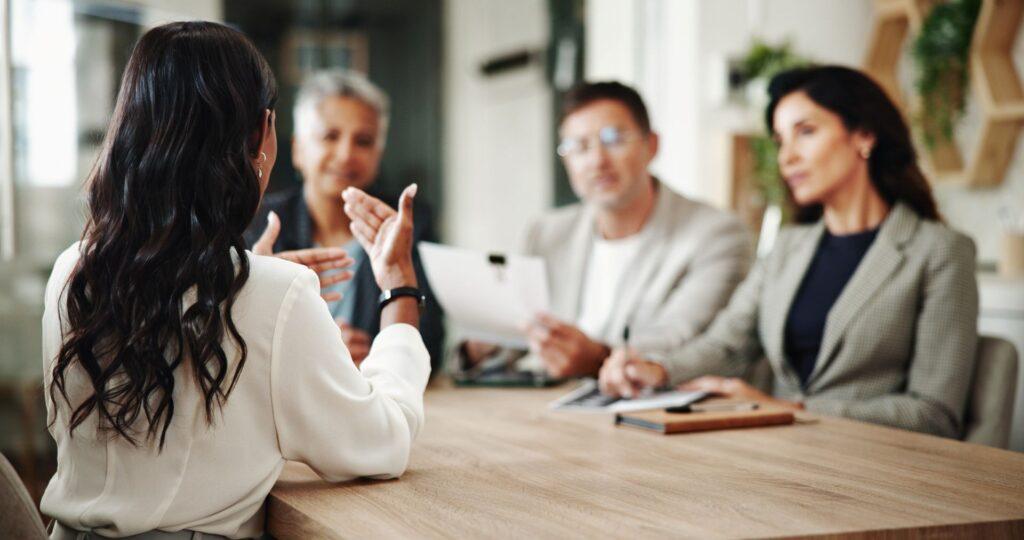 Vier Personen im Gespräch über Cybersicherheit und NIS 2 Beratung; Fokus auf eine Frau in Managementkleidung – symbolisiert Entscheidungsprozesse im Unternehmen.